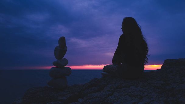 Silhouette d'une femme équilibrant rochers et pierres sur la côte océanique au coucher du soleil heure du lever du soleil. - Photo, image