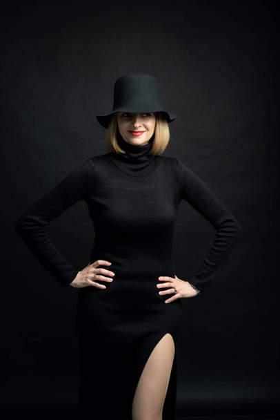 beautiful young woman in black dress and hat posing on dark background - Foto, imagen