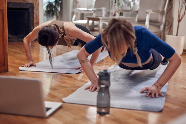 Pretty women working out at home. Adult ladies with beautiful shaped bodies exercising in the apartment. - 写真・画像