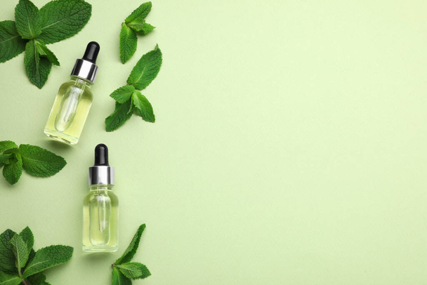 Bottles of essential oil and mint on light green background, flat lay. Space for text - Фото, зображення