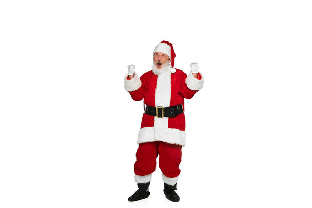 Portret van senior man in beeld van de Kerstman poseren met winnende emoties geïsoleerd over witte achtergrond. Concept van fictief karakter, vakantie, Nieuwjaar, Kerstmis. Kopieer ruimte voor advertentie - Foto, afbeelding