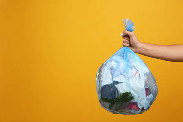 Женщина держит полный мешок для мусора на желтом фоне, крупным планом. Пространство для текста - Фото, изображение