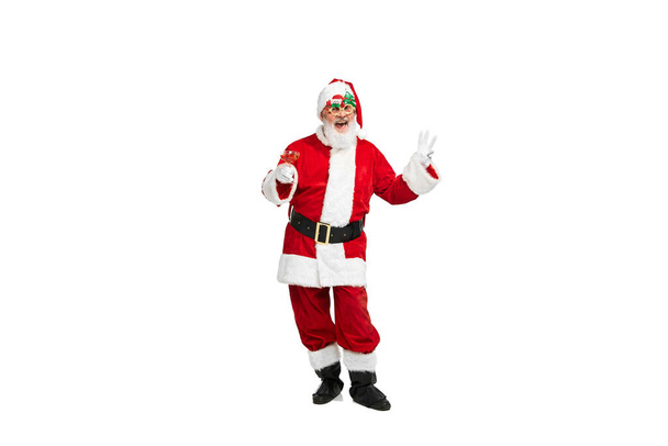 Portrait of happy senior man in image of Santa Claus in festive glasses posing isolated over white background. Concept of fictional character, holiday, New Year, Christmas. Copy space for ad - Photo, Image