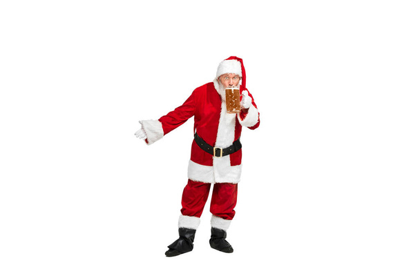 Portrait of senior man in image of Santa Claus sipping lager foamy beer isolated over white background. Concept of fictional character, holiday, New Year, Christmas. Copy space for ad - Photo, Image