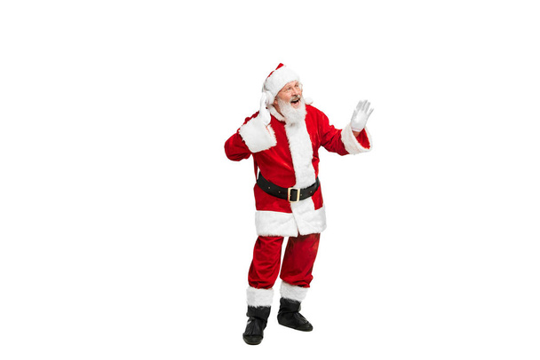 Porträt eines älteren Mannes im Bild des Weihnachtsmannes, der über Kopfhörer isoliert vor weißem Hintergrund Musik hört. Konzept der fiktionalen Figur, Urlaub, Neujahr, Weihnachten. Kopierraum für Werbung - Foto, Bild