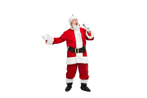 Retrato del hombre mayor en imagen de Santa Claus cantando en micrófono aislado sobre fondo blanco. Hora de la fiesta. Concepto de carácter ficticio, día festivo, Año Nuevo, Navidad. Copiar espacio para anuncio - Foto, imagen