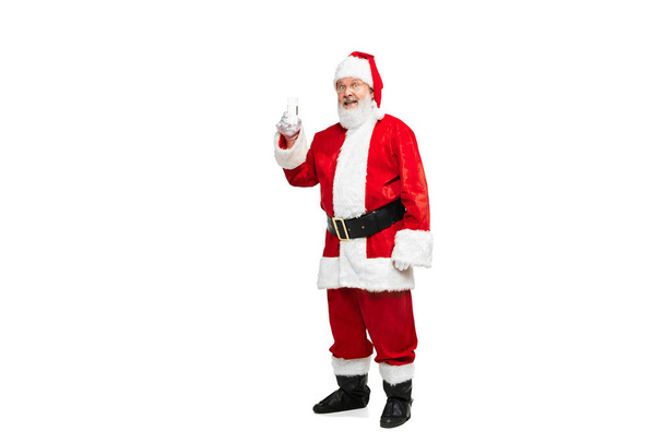Portrait of senior man in image of Santa Claus posing with glass of water isolated over white background. Concept of fictional character, holiday, New Year, Christmas. Copy space for ad - Photo, Image