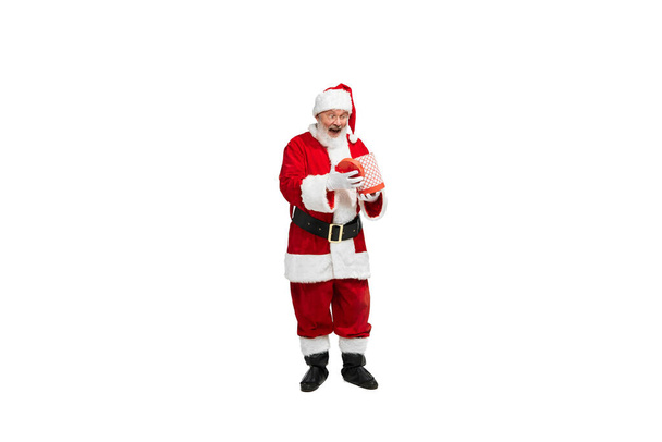 Portret van senior man in beeld van de Kerstman met huidige doos geïsoleerd over witte achtergrond. Emoties van verrassing. Concept van fictief karakter, vakantie, Nieuwjaar, Kerstmis. Kopieer ruimte voor advertentie - Foto, afbeelding