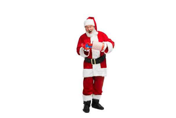 Portrait of senior man in image of Santa Claus with present box for kids isolated over white background. Concept of fictional character, holiday, New Year, Christmas. Copy space for ad - Photo, Image