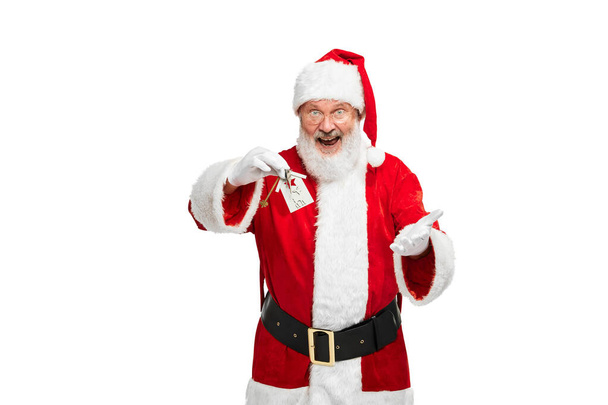 Portrait of senior man in image of Santa Claus with new apartment keys isolated over white background. Housewarming. Concept of fictional character, holiday, New Year, Christmas. Copy space for ad - Photo, Image