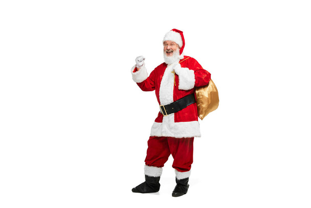 Portrait of senior man in image of Santa Claus posing with big golden box for presents isolated over white background. Concept of fictional character, holiday, New Year, Christmas. Copy space for ad - Photo, Image