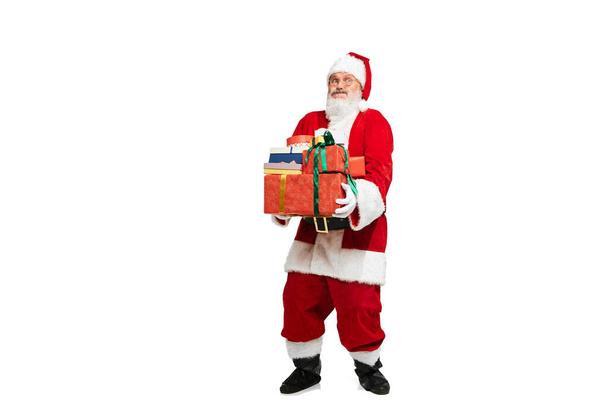 Portrait of senior man in image of Santa Claus with present box isolated over white background. Heavy gifts. Concept of fictional character, holiday, New Year, Christmas. Copy space for ad - Photo, Image