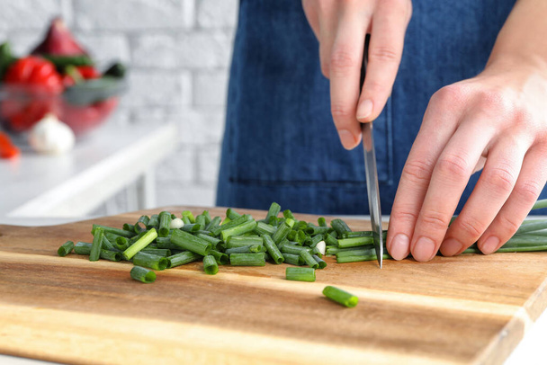 Woman cutting green spring onion on wooden board, closeup - Photo, image