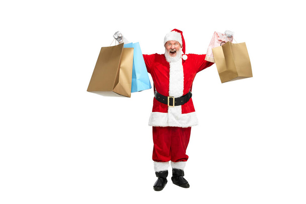 Portrait of senior man in image of Santa Claus with many shopping bags isolated over white background. Big Friday sales. Concept of fictional character, holiday, New Year, Christmas. Copy space for ad - Photo, Image