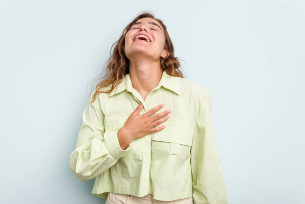 Young caucasian woman isolated on blue background laughs out loudly keeping hand on chest. - Foto, Imagem