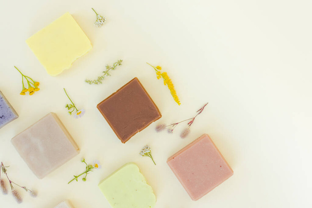 Handmade vegan soap made with natural herbal ingredients, herbs and flowers over light yellow background with copy space. Making skincare products at home. Flat lay style  - Foto, immagini