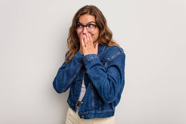Mladá běloška izolovaná na modrém pozadí, která se něčemu směje, zakrývá ústa rukama. - Fotografie, Obrázek