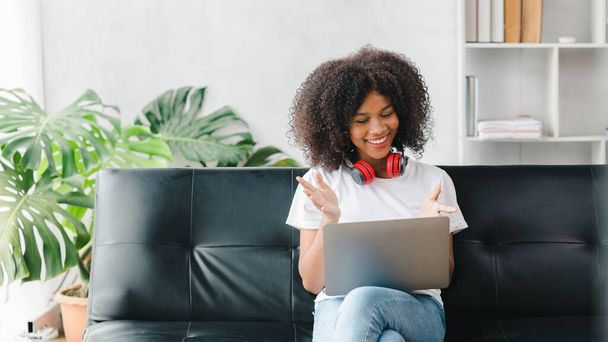 Een Amerikaanse vrouw zit op een bank op een laptop, videogesprekken met vrienden, brengt haar weekend door op sociale media, kijkt films en luistert thuis naar muziek. Vakantie concept. - Foto, afbeelding