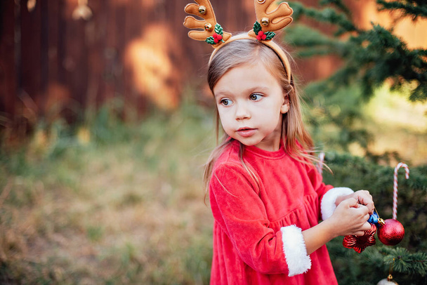 Kerstmis in juli. Kind wachtend op Kerstmis in juli in hout. portret van een meisje dat kerstboom versiert. wintervakantie en mensen concept. Vrolijk kerstfeest en fijne feestdagen. - Foto, afbeelding