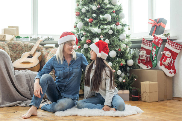 Frohe Weihnachten und frohe Feiertage. Fröhliche Mutter und ihre süße Tochter tauschen Geschenke aus. Mutter und kleines Kind vergnügen sich in der Nähe von Bäumen. Liebevolle Familie mit Geschenken im Zimmer. - Foto, Bild