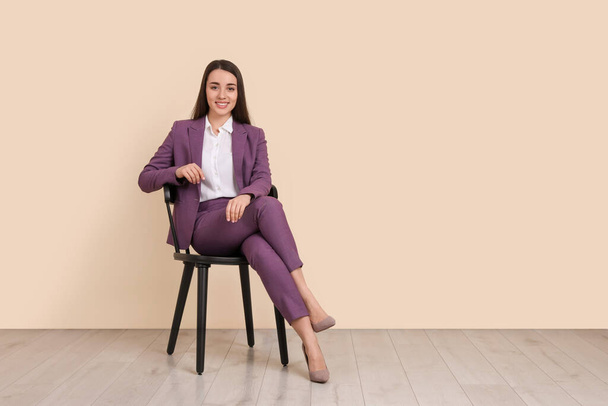 Young businesswoman sitting on chair near beige wall in office, space for text - Fotografie, Obrázek