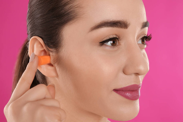 Young woman inserting foam ear plug on pink background, closeup - Foto, Bild