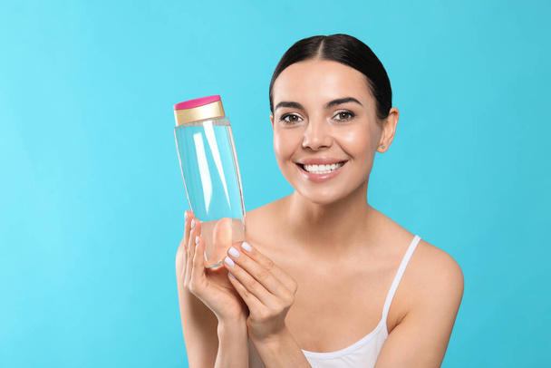 Young woman with bottle of micellar water on light blue background - Foto, Imagem