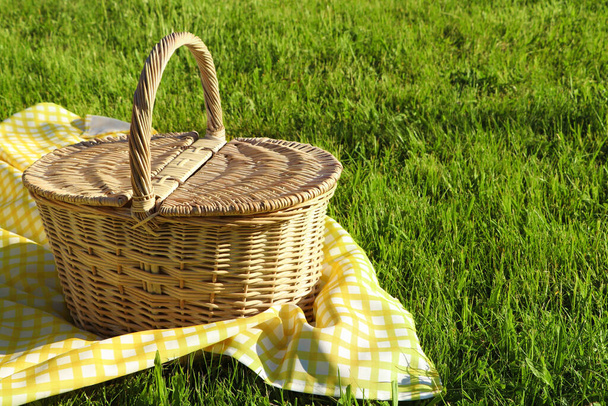 Picnic basket with checkered tablecloth on green grass outdoors, space for text - Фото, изображение