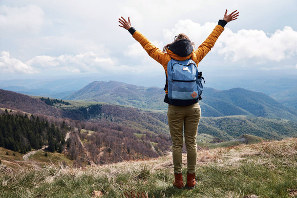 Young woman with rucksack and arms wide opened on the top of the hilly landscape. - Photo, Image