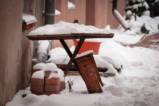 Gros plan d'une petite table et d'un banc dans une cour avec une pile de briques rouges debout à proximité et recouverte de neige blanche - Photo, image