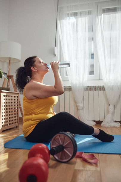 Woman training inside the living room, exercising at home, pause and drinking water. - Fotó, kép