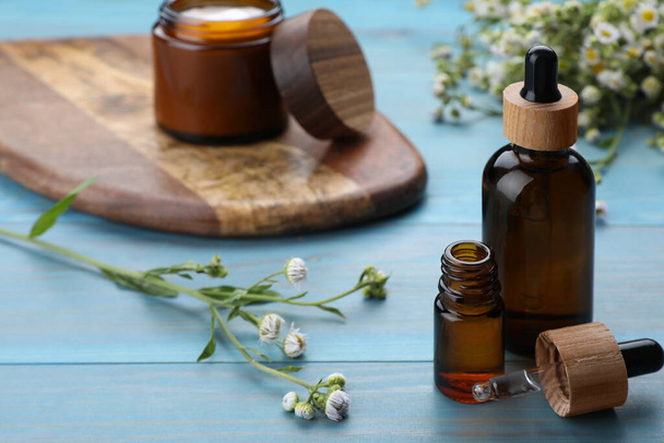 Bottles of essential oil with chamomile flowers on light blue wooden table, closeup. Space for text - Фото, зображення