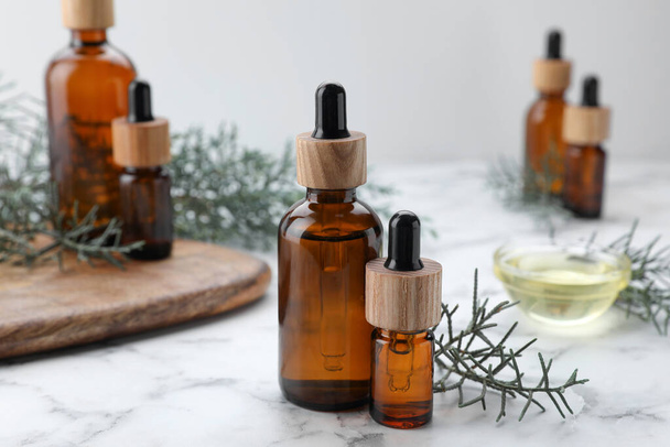 Bottles of juniper essential oil and twigs on white marble table - Photo, image