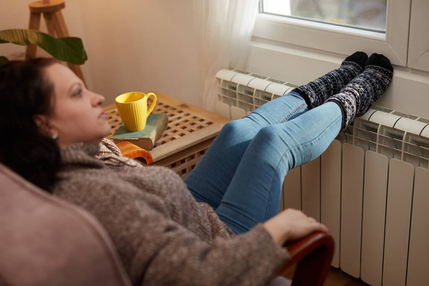 Soğuk bir kış gününde ayakları ısıtan kadın, enerji ve gaz krizi, soğuk oda, ısıtma sorunları. - Fotoğraf, Görsel