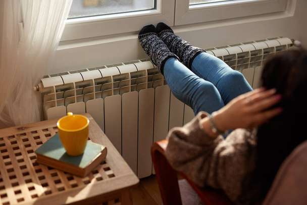 Женщина нагревает ноги в холодный зимний день, энергетический и газовый кризис, холодная комната, проблемы с отоплением. - Фото, изображение