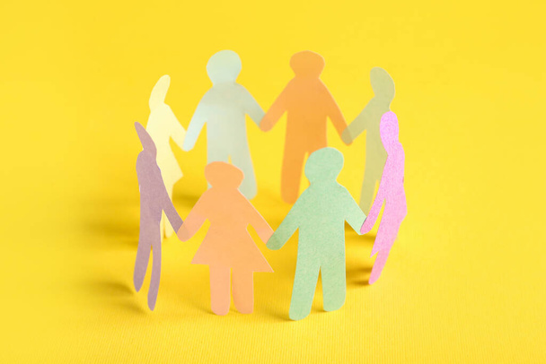 Many different paper human figures standing in circle on yellow background. Diversity and inclusion concept - Фото, изображение