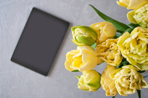 Top view of a bouquet of beautiful yellow tulips with dew drops in a glass vase and a tablet. - Valokuva, kuva