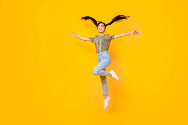 Full length picture of energetic young lady jumping up flying hair two ponytails hairstyle isolated on yellow color background. - Foto, Imagem
