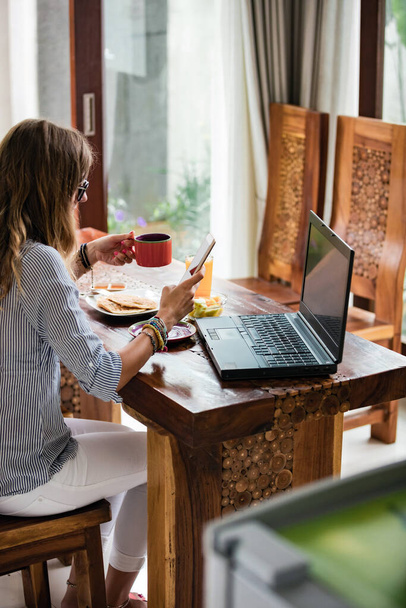 Jonge volwassen vrouw met smartphone en laptop, werken vanuit huis concept. - Foto, afbeelding