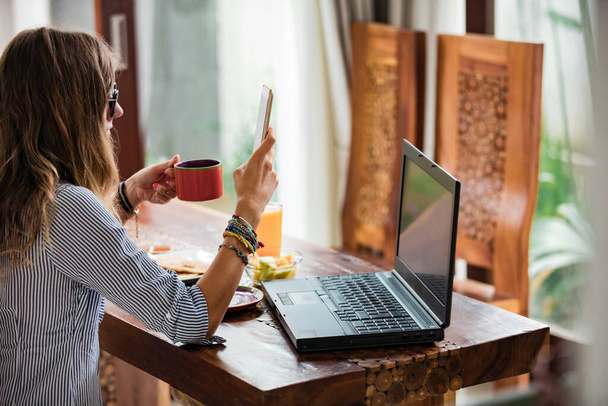 Giovane donna adulta utilizzando smartphone e laptop, lavorando dal concetto di casa. - Foto, immagini