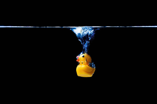 Close-up of a toy yellow duck falling underwater isolated on black background. - Photo, image