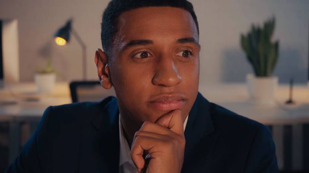 Homme d'affaires afro-américain pensif regardant loin dans le bureau la nuit - Photo, image