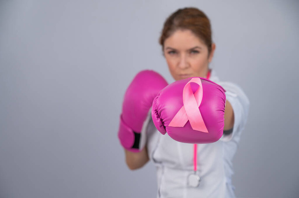 Female doctor in pink boxing gloves with a pink ribbon on a gray background. Fight against breast cancer - Фото, изображение