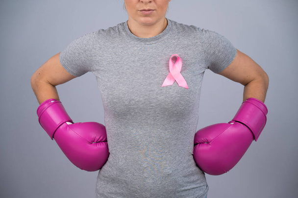 A faceless woman in pink boxing gloves with a pink ribbon holds her hands at her hips. Fight against breast cancer - Φωτογραφία, εικόνα