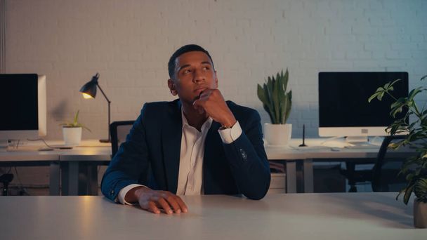 Pensativo hombre de negocios afroamericano en traje mirando hacia otro lado en la oficina por la noche  - Foto, Imagen