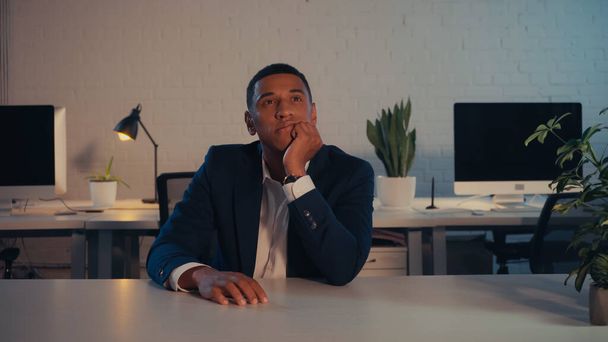 Homme d'affaires afro-américain réfléchi assis à table au bureau la nuit  - Photo, image