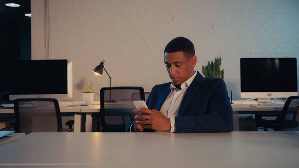 Afroamerikanischer Geschäftsmann im Anzug nutzt Handy nachts im Büro  - Foto, Bild