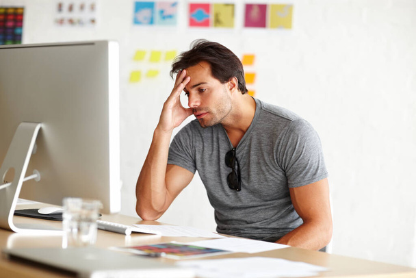 Sufriendo de bloqueo de escritores. Un hombre guapo sentado en un escritorio y mirando una pantalla de computadora con la cabeza apoyada en su mano - Foto, imagen