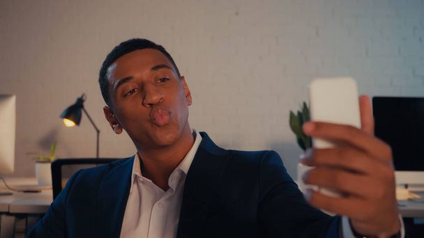 Hombre de negocios afroamericano haciendo pucheros mientras toma selfie en el teléfono inteligente en la oficina  - Foto, Imagen