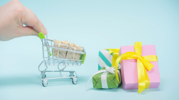 cropped view of man holding small shopping cart near wrapped presents on blue background  - Foto, Bild